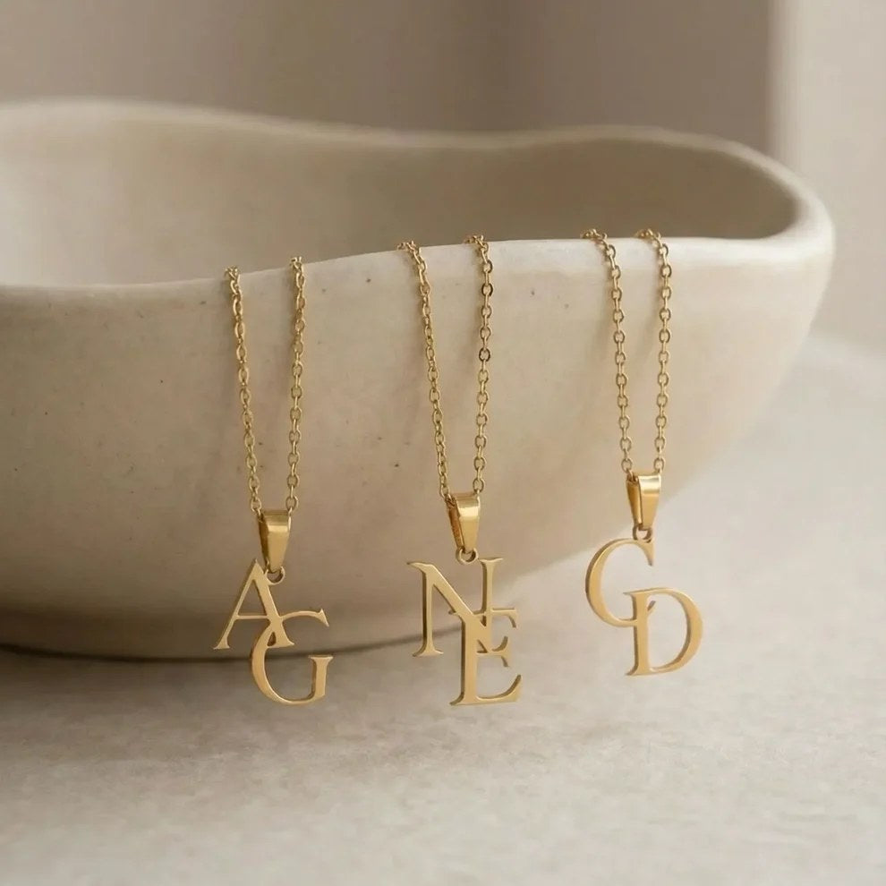 Tre initialhalsband i guld med monogrammen AG, NE och GD