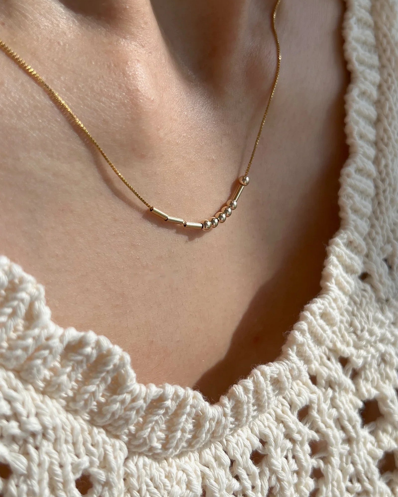 Morsekodshalsband i guld mot strikad topp